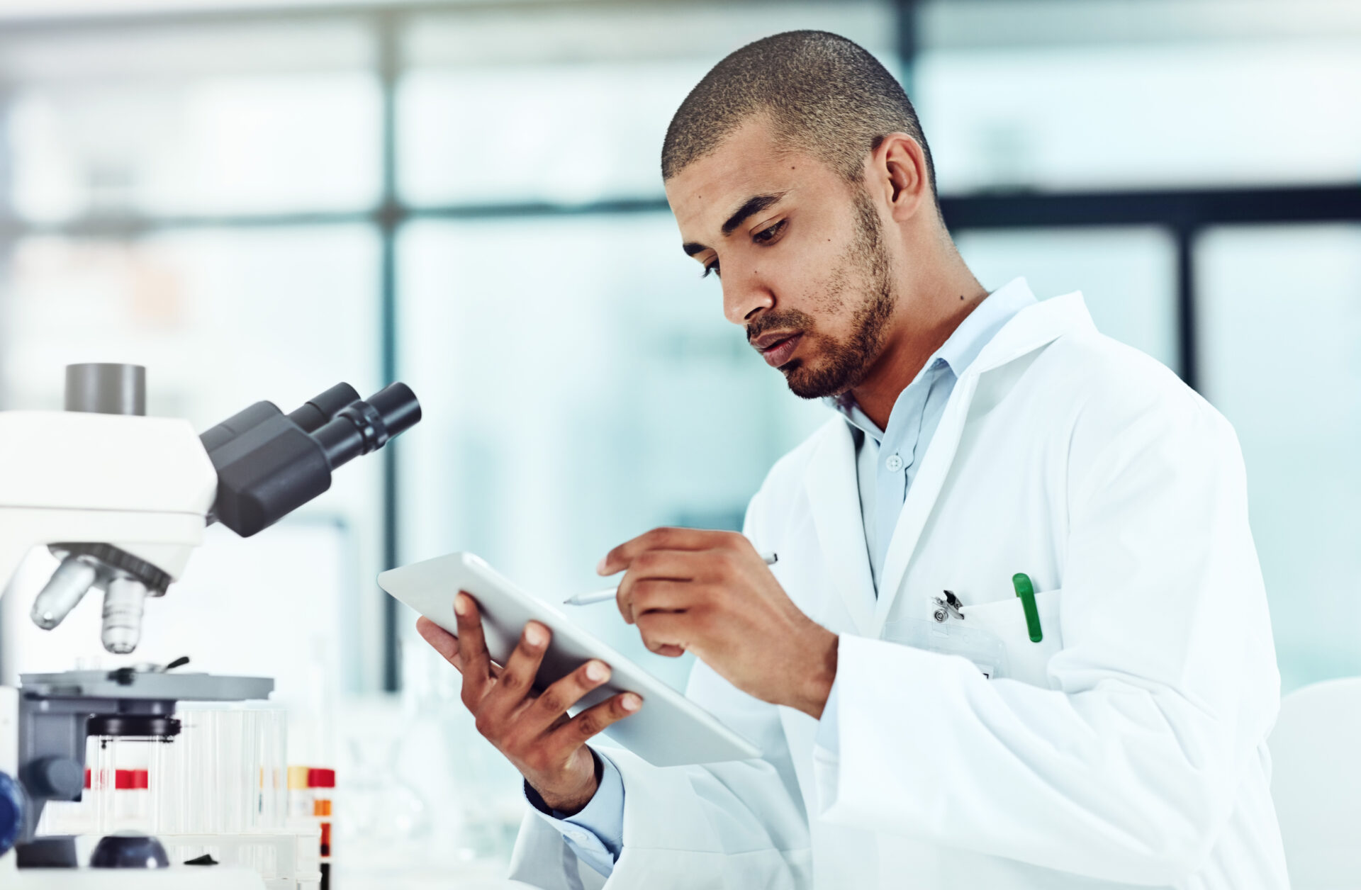 Serious male scientist working on a tablet reviewing an online phd publication in a lab. Laboratory worker updating health data for a science journal. Medical professional document clinical trial AdobeStock 522372045